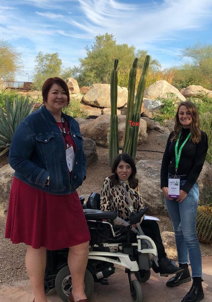 A photo of Tricia Jones-Parkin standing, Kelie Hess, and Aubrey Snyder. They are outside in Phoenix, Arizona by a tall cactus with desert landscaping and blue skies in the background.